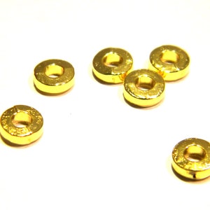 May include: Six gold-colored metal rings, each with a circular hole in the center. The rings are arranged in a semi-circle on a white surface.