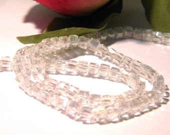 May include: A strand of clear glass beads with a square shape. The beads are iridescent and have a subtle sparkle.