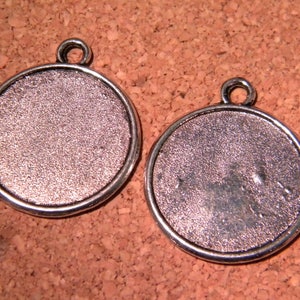 Peut inclure: Deux pendentifs ronds en métal argenté avec une surface lisse légèrement texturée. Chaque pendentif a une boucle en haut pour l'attacher à une chaîne ou un cordon.