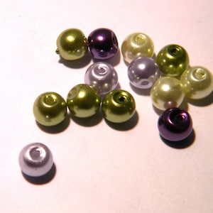 May include: A collection of assorted beads in various colors, including purple, green, and white. The beads are round and have a smooth, glossy finish.