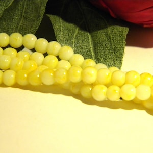 Puede incluir: Una hebra de cuentas de vidrio amarillas y blancas. Las cuentas son redondas y tienen un patrón moteado.
