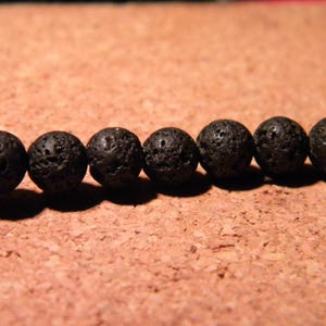 May include: A strand of black lava rock beads. The beads are round and have a rough, textured surface.
