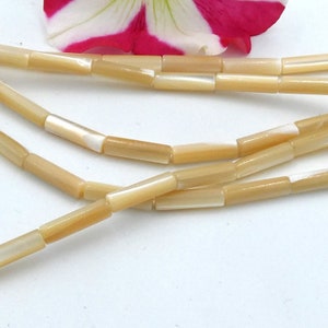 Può includere: Una collana di perline di conchiglia beige e bianche, ogni perlina ha la forma di un tubo rettangolare.