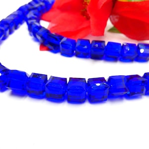 May include: A strand of bright blue faceted square glass beads. The beads are strung on a clear thread and are arranged in a straight line.