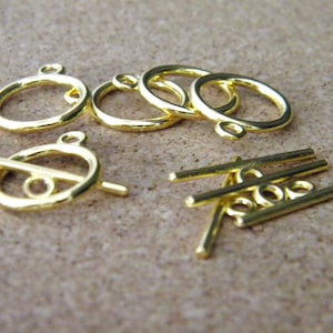 May include: Gold-toned metal clasps and toggle closures for jewelry making. The clasps are round with a loop on top, and the toggles have a bar that slides through the loop.