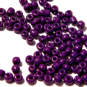May include: A large quantity of small, round, purple beads. The beads are scattered on a white surface.