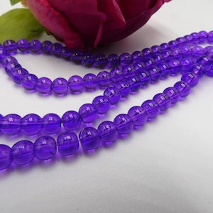 May include: A strand of purple glass beads. The beads are round and have a slight shine to them.