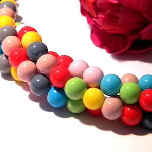 Peut inclure: Un brin de perles rondes colorées dans différentes couleurs, notamment rouge, jaune, bleu, vert et gris. Les perles sont enfilées sur un fil transparent.