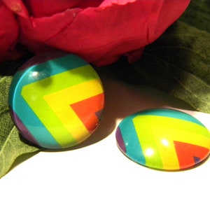 Könnte beinhalten: Zwei runde, farbenfrohe, dekorative Knöpfe mit einem Regenbogen-Chevron-Muster. Die Knöpfe sind türkis, gelb, rot und lila.