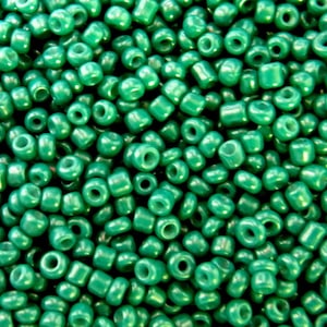 May include: A close-up image of a large quantity of small, round, green beads. The beads have a slightly iridescent finish.