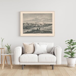 Pode incluir: Uma ilustra&ccedil;&atilde;o vintage em preto e branco de uma cidade com uma montanha ao fundo. A ilustra&ccedil;&atilde;o est&aacute; emoldurada e pendurada em uma parede branca acima de um sof&aacute; branco.