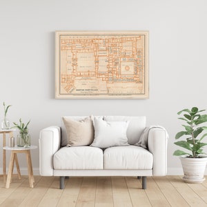 May include: A vintage map of Hampton Court Palace, printed in orange and black on a cream background, framed in a light wood frame. The map shows the layout of the palace, including the various rooms and courtyards.