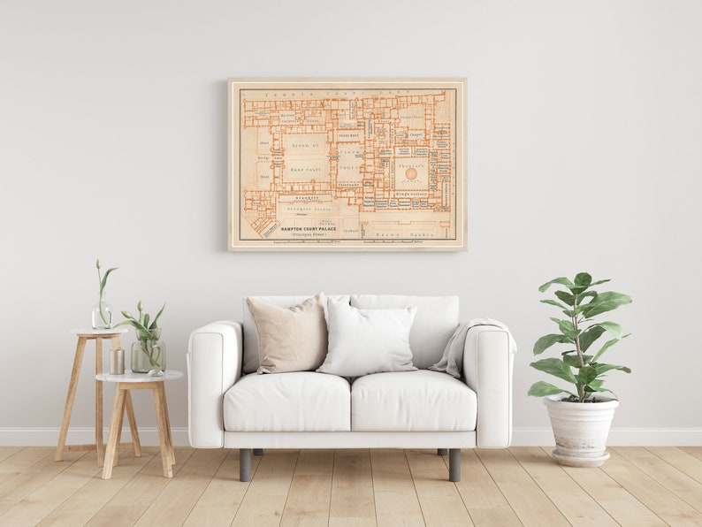 May include: A vintage map of Hampton Court Palace, printed in orange and black on a cream background, framed in a light wood frame. The map shows the layout of the palace, including the various rooms and courtyards.