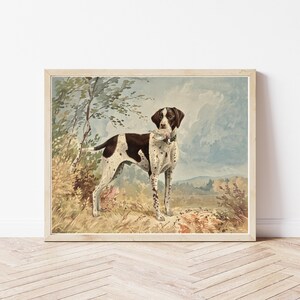 May include: Framed vintage print of a Pointer dog in a field. The dog has a brown and white coat, with a brown head and ears. The background features a landscape with trees, bushes, and a cloudy sky. The artwork is in a wooden frame.