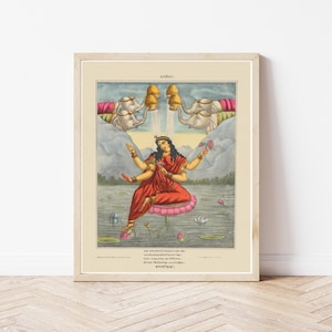 May include: Framed print depicting a Hindu deity seated on a lotus flower in a lake. The artwork uses vibrant colours, with the deity in red clothing, and two elephants pouring water above. The print is in a light-coloured wooden frame.