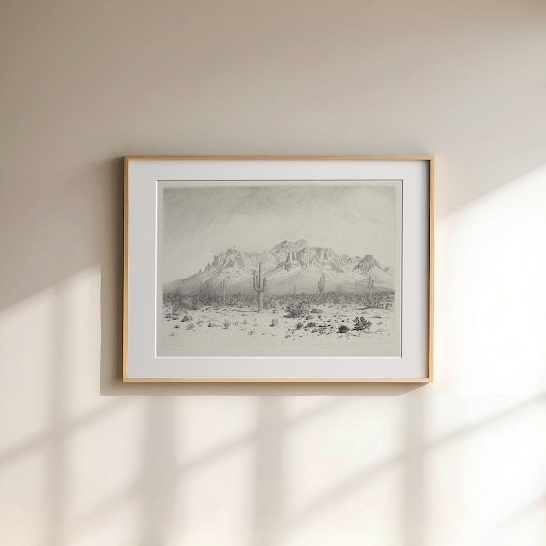Puede incluir: Un dibujo en blanco y negro de un paisaje des&eacute;rtico con monta&ntilde;as en el fondo y algunos cactus en primer plano. El dibujo est&aacute; enmarcado en un marco de madera claro.