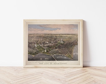 May include: A framed vintage map print of Washington, D.C., showing a detailed aerial view of the city. The print has a beige frame and is set against a white wall and a wooden floor. The title "THE CITY OF WASHINGTON" is visible.
