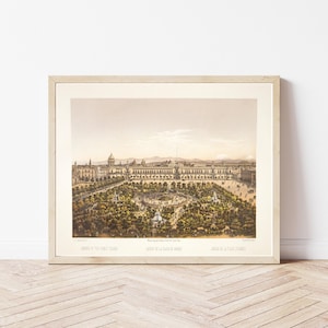 May include: Framed vintage print of a European city with a large building and a park. The print is in a light wood frame and features a sepia-toned image with green and brown accents. The print is titled "Jardins de la Place de Armes".