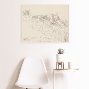 May include: A black and white line drawing of a castle on a hill with trees. The drawing is framed and hanging on a white wall. The text "The Alcazaba from the East of Malaga" is written below the drawing.