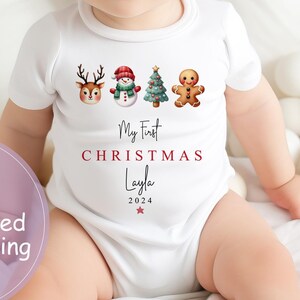 May include: White baby onesie with a red, green, and brown Christmas design. The onesie says "My First Christmas Layla 2024" with a red star.
