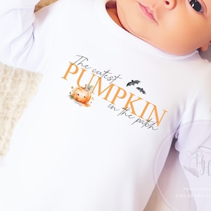 May include: White long-sleeve baby onesie with the text "The cutest pumpkin in the patch" in orange and black. A small pumpkin with a face is illustrated next to the text.
