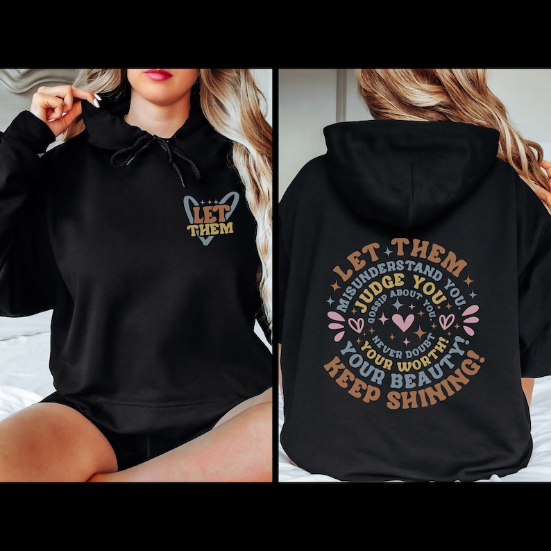 Puede incluir: Sudadera con capucha negra con el texto "LET THEM" en la parte delantera. La parte trasera muestra un dise&ntilde;o circular con las palabras "LET THEM MISUNDERSTAND YOU, JUDGE ABOUT YOU, NEVER DOUBT YOUR WORTH, KEEP SHINING!" con corazones y estrellas.