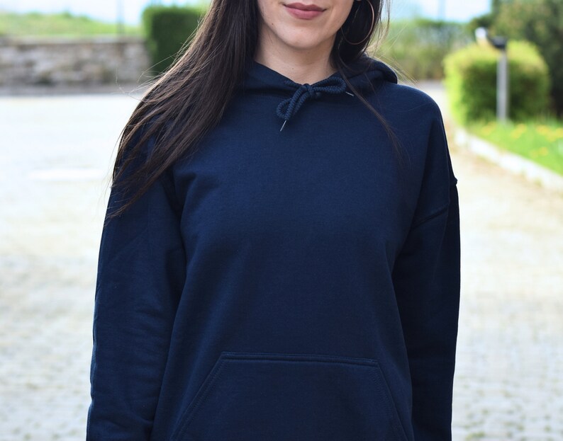 Puede incluir: Una sudadera con capucha azul marino con capucha con cord&oacute;n y bolsillo delantero. La sudadera est&aacute; hecha de un material suave y tiene un ajuste relajado. La imagen muestra la parte superior del cuerpo de una persona que lleva la sudadera con capucha.