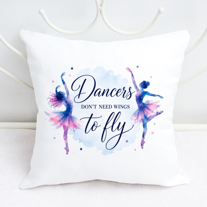 A white square pillow with two watercolor ballerinas and the text "Dancers don't need wings to fly" rests against a white metal headboard.