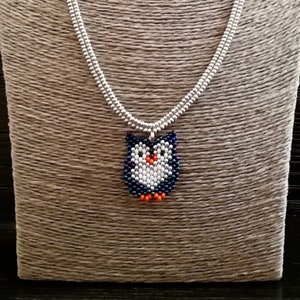Op de afbeelding: Een zilveren ketting met een kralen uil hanger. De uil is blauw, wit en oranje.