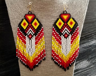 May include: A pair of long, beaded earrings with a geometric pattern in red, yellow, black, and white. The earrings have a fringe of beads at the bottom.