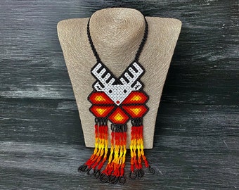 May include: A beaded necklace with a geometric deer design in black, white, and red. The necklace has long, colorful tassels in shades of orange, yellow, and red.