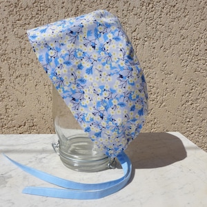 May include: A blue and white floral patterned surgical cap with blue ties. The cap is made of cotton fabric and has a gathered design at the top.