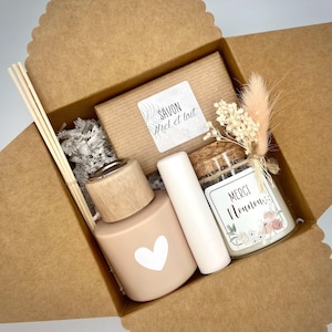 Peut inclure: Coffret cadeau contenant un diffuseur rose avec un cœur blanc, un baume à lèvres, une petite bougie, un pain de savon et des bâtonnets décoratifs. Le savon porte l'étiquette "Savon Miel et Lait". La bougie porte l'étiquette "Merci Nounou".