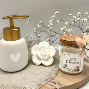 Peut inclure: Un distributeur de savon en céramique blanche avec une pompe dorée et un cœur, un savon blanc en forme de rose et une bougie dans un bocal en verre avec un couvercle en liège. La bougie porte l'inscription "SUPER Marraine".