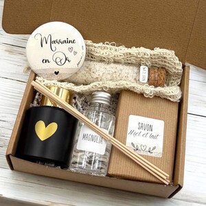 Op de afbeelding: Een geschenkdoos met een zwarte diffuser met een gouden hart, een fles met het label "Magnolia", een stuk zeep, een ronde badge met tekst en een fles badzout. De doos is bruin.