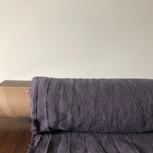 May include: A roll of dark purple linen fabric on a wooden surface. The fabric is folded and has a rough texture.