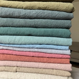 Pode incluir: Uma pilha de 14 amostras de tecido de linho em várias cores, incluindo verde, azul, rosa, bege e branco.