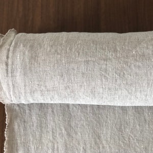 Puede incluir: Un rollo de tela de lino gris claro. La tela está tejida con una textura sutil y tiene un tacto ligeramente áspero.