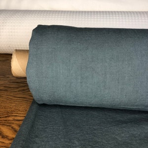 May include: A roll of dark blue linen fabric. The fabric is tightly rolled and has a smooth, even texture.