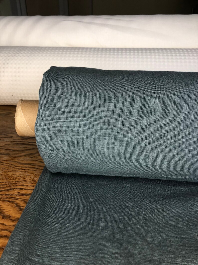 May include: A roll of dark blue linen fabric. The fabric is tightly rolled and has a smooth, even texture.