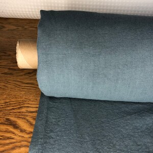 May include: A roll of blue linen fabric on a wooden surface. The fabric has a subtle texture and a slightly darker shade at the edges.