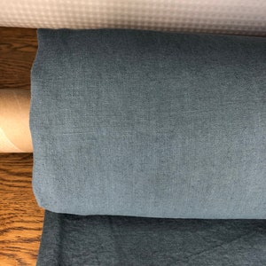 May include: A roll of dark gray fabric with a subtle texture. The fabric is rolled up and sitting on a wooden surface.
