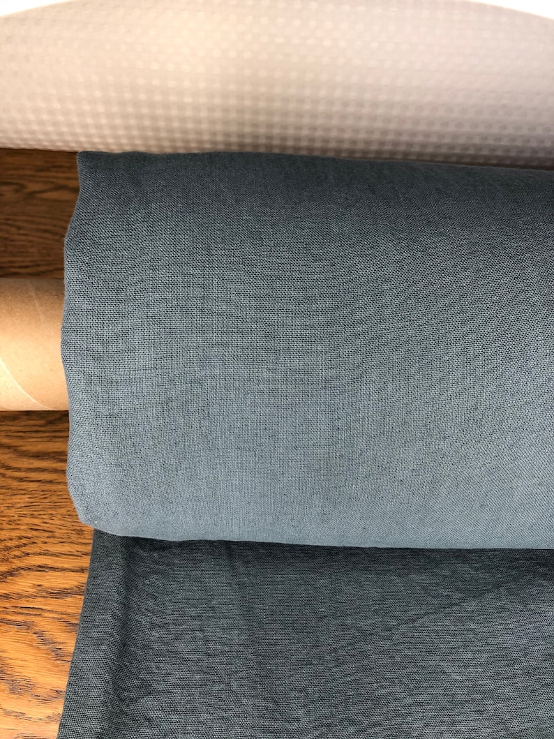 May include: A roll of dark gray fabric with a subtle texture. The fabric is rolled up and sitting on a wooden surface.