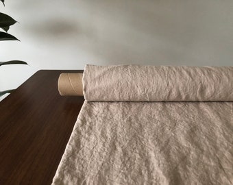 May include: A roll of natural linen fabric on a wooden surface. The fabric is a light beige color and has a textured, slightly wrinkled appearance.