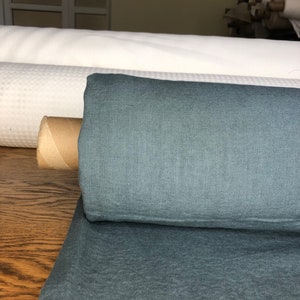 May include: A roll of teal blue linen fabric. The fabric is folded and rolled up, with a brown cardboard tube at the center.