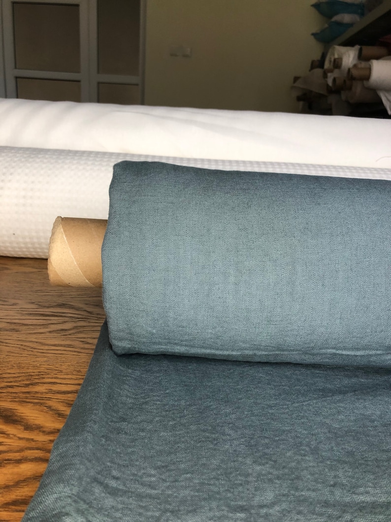 May include: A roll of teal blue linen fabric. The fabric is folded and rolled up, with a brown cardboard tube at the center.