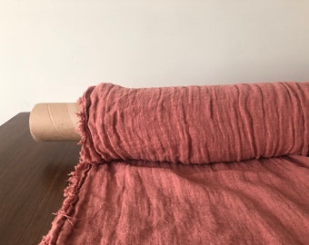 May include: A roll of dusty rose colored linen fabric with raw edges. The fabric is rolled on a cardboard tube.