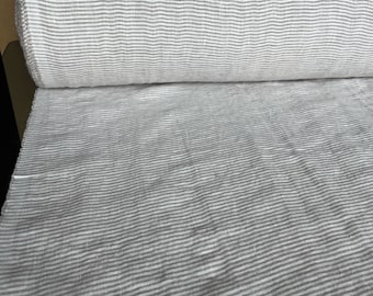 Puede incluir: Un rollo de tela de lino blanco con finas rayas grises. La tela está tejida con una textura sutil.