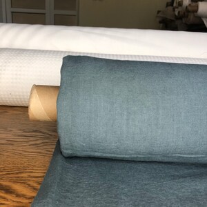 May include: A roll of dark teal linen fabric. The fabric has a textured, woven look and is rolled up on a cardboard tube.
