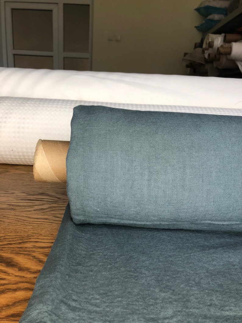 May include: A roll of dark teal linen fabric. The fabric has a textured, woven look and is rolled up on a cardboard tube.